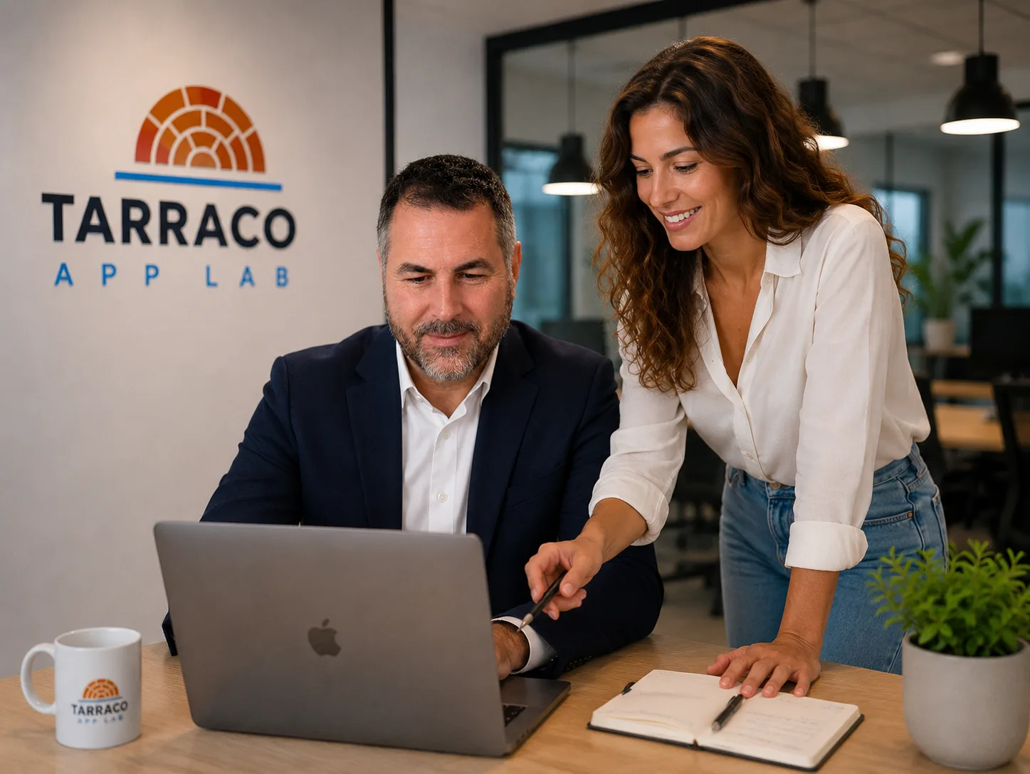 Dos integrantes del equipo de Tarraco App Lab colaboran ante un portátil en la oficina, junto al logotipo de la marca